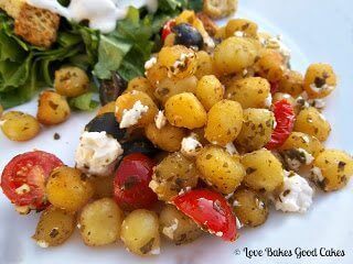 Crispy Pesto Gnocchi with Tomatoes, Black Olives and Feta Cheese with green salad on white plate