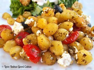 Crispy Pesto Gnocchi with Tomatoes, Black Olives and Feta Cheese with green salad on white plate close up