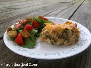 Tuna Noodle Casserole with green salad and red tomatoes with croutons on white plate.