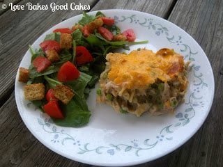 Tuna Noodle Casserole with green salad and red tomatoes with croutons on white plate top view.