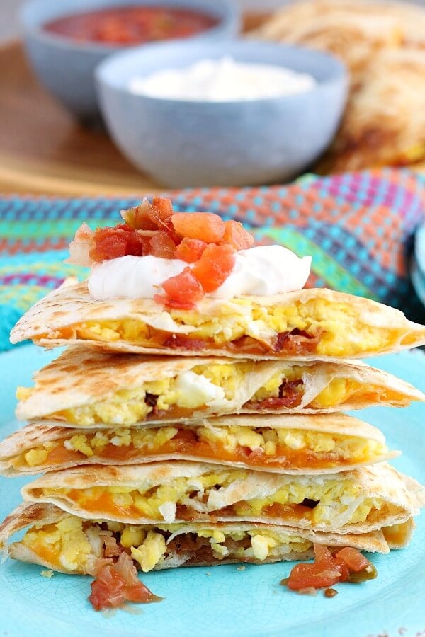 This stack of egg quesadillas is finished and ready to be eaten, topped with sour cream and salsa. 