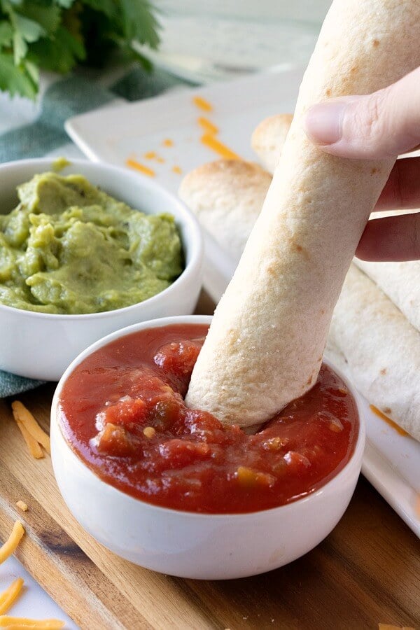 jalapeno popper chicken taquito being dipped into salsa with guacamole in background