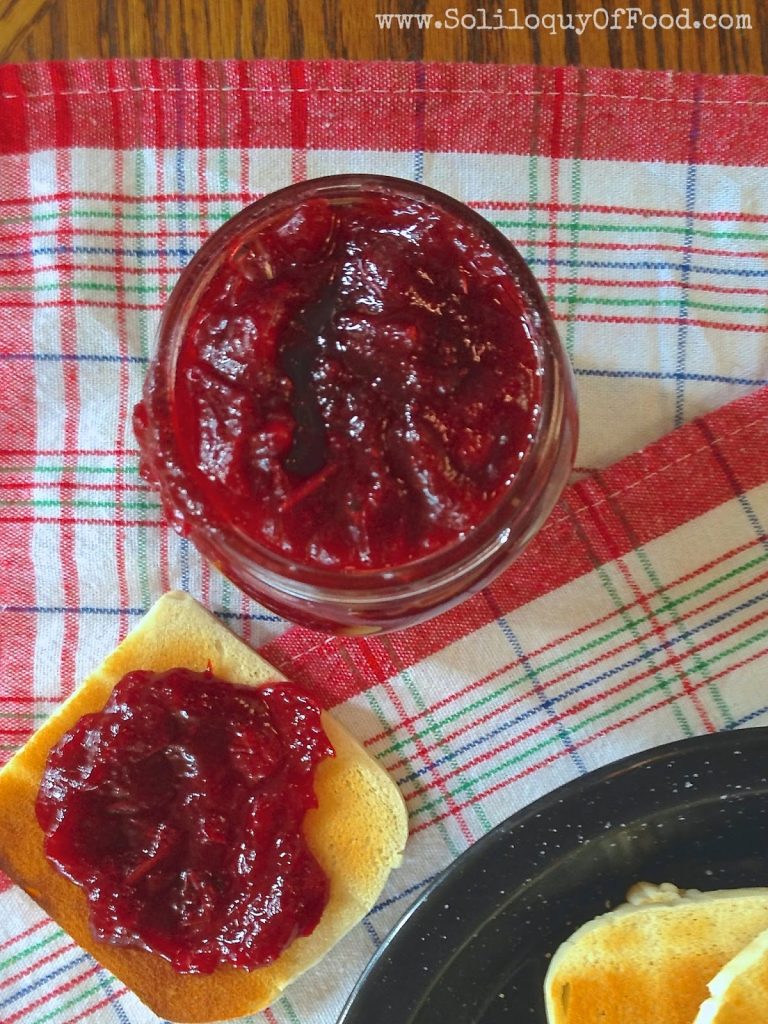Cranberry Jam in a jar with some spread on a piece of toast.