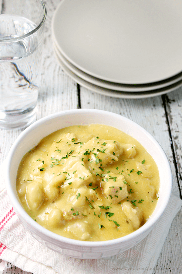 Slow Cooker Chicken and Dumplings in a bowl with a stack of plates.