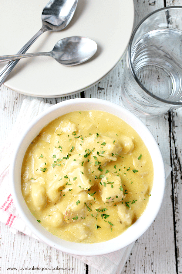 Slow Cooker Chicken and Dumplings in a white bowl with plates and spoons.