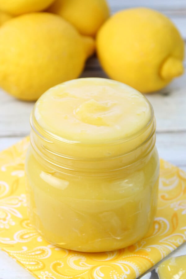 lemon curd in glass jar with lemons in background
