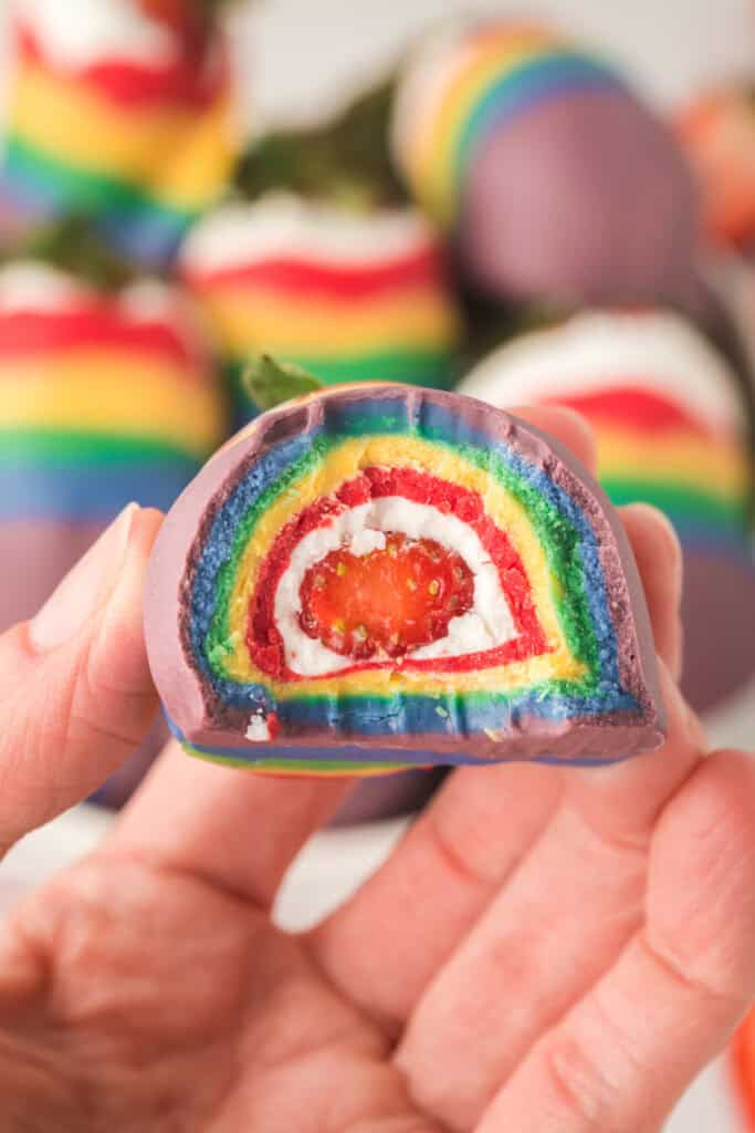 hand holding a rainbow strawberry with a cross section showing the different layers of colors