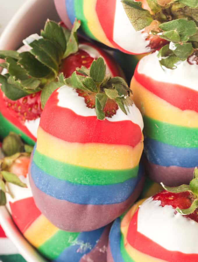 closeup of rainbow candy coated strawberries stacked in bowl