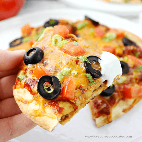 Person holding a slice of Mexican pizza with sour cream on top.