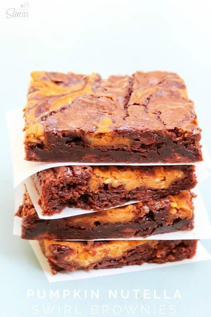 Pumpkin Nutella Swirl Brownies stacked up with parchment paper.