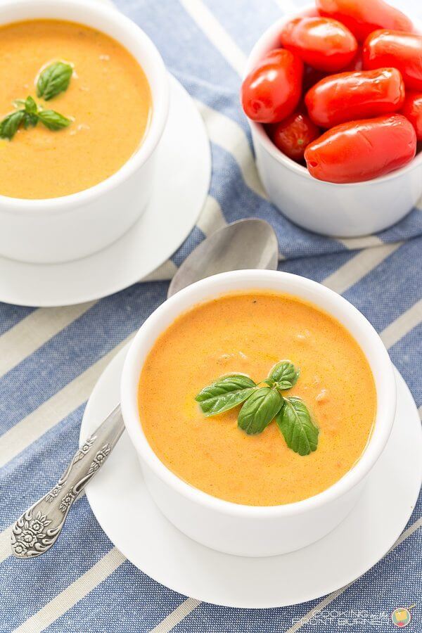 Creamy Tomato and Basil in two bowls with a spoon and a bowl of fresh tomatoes.
