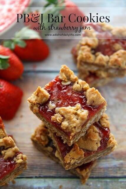  PB&J Bars with Strawberry Jam stacked up on a cutting board with fresh strawberries.