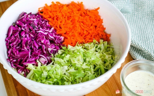 Purple and green cabbage and carrots in a mixing bowl for a coleslaw recipe.