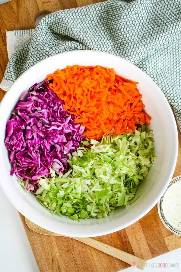 Purple and green cabbage and carrots in a mixing bowl for a coleslaw recipe.