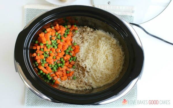 Carrots, peas and cheese added to a slow cooker for chicken and rice.