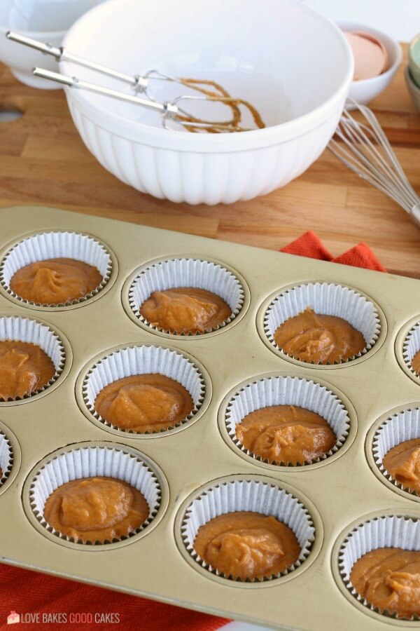 Pumpkin muffin batter divided into cupcake liners in a baking sheet.
