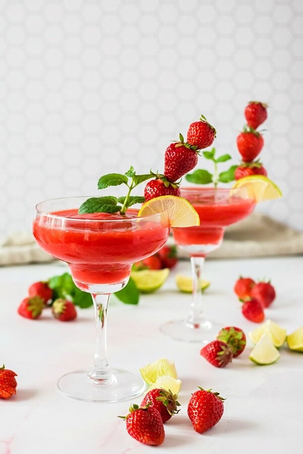 two glasses of strawberry daiquiri garnished with fruit and mint