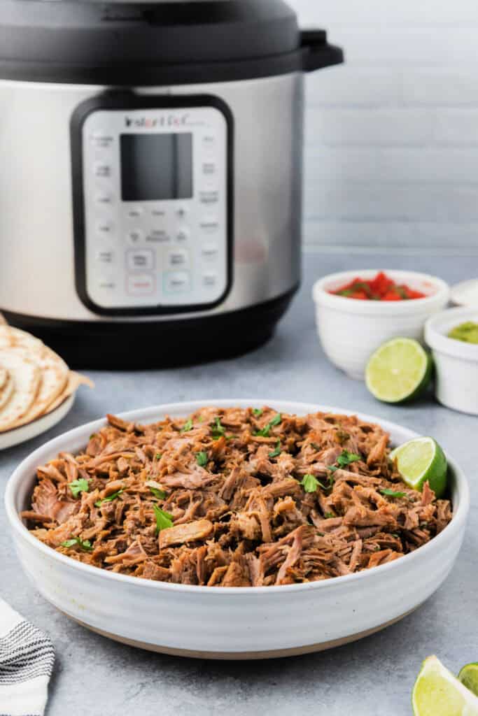 bowl of carnitas meat in front of an instant pot