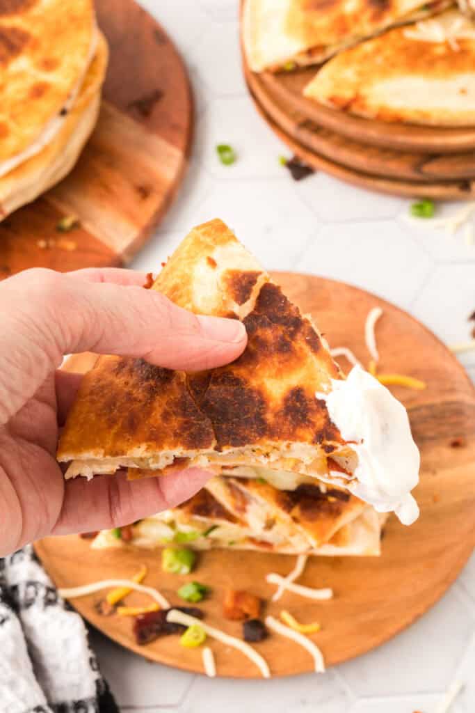 hand holding a loaded baked potato quesadilla that was dipped in sour cream