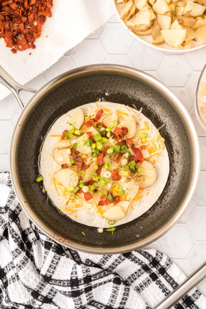 layers of a loaded baked potato quesadilla in a skillet before the top tortilla goes on