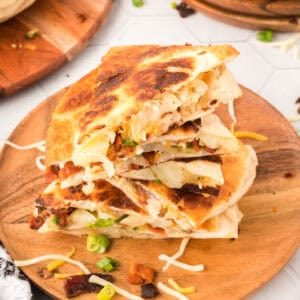 closeup of loaded baked potato quesadilla pieces stacked on wooden cutting board