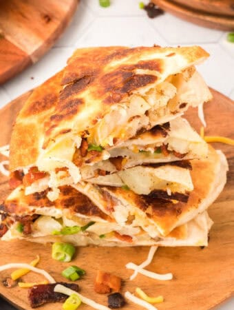 closeup of loaded baked potato quesadilla pieces stacked on wooden cutting board