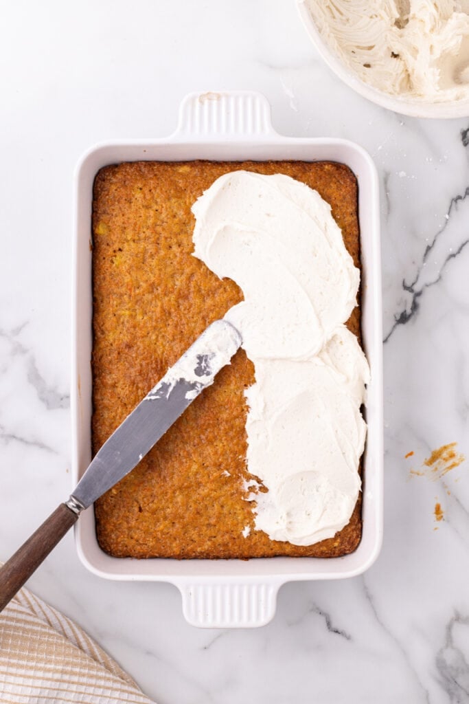 frosting being spread over carrot cake