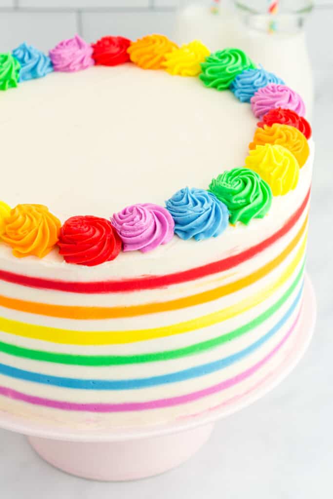 baked and frosted rainbow striped funfetti cake on cake stand